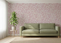 Dusty Rose Vines wallpaper of pink foliage on cream behind a sage green sofa and potted plant in a living room