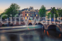 Dutch Canal Dreams wallpaper mural shown as a close-up of Amsterdam canal houses and lit stone bridges at dusk