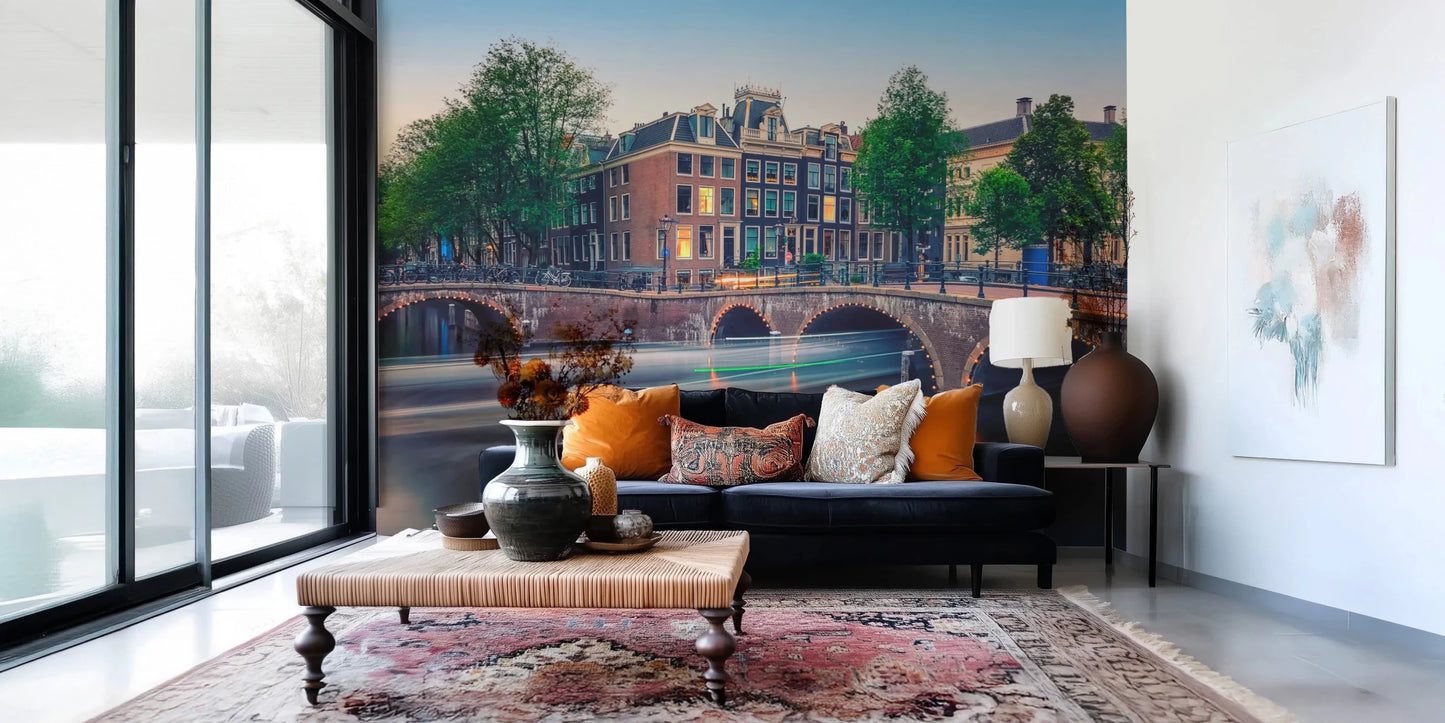 Dutch Canal Dreams wallpaper mural of dusk-lit canal houses above a navy sofa with orange pillows in a living room