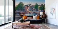 Dutch Canal Dreams wallpaper mural of dusk-lit canal houses above a navy sofa with orange pillows in a living room
