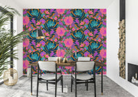 Exotic Bloom wallpaper behind a wood dining table and grey chairs beside stacked firewood and a palm