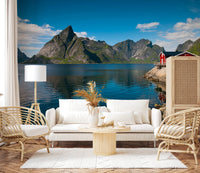 Fishing huts wallpaper mural of a blue fjord with grey mountains and red huts behind a white sofa and rattan chairs in a living room