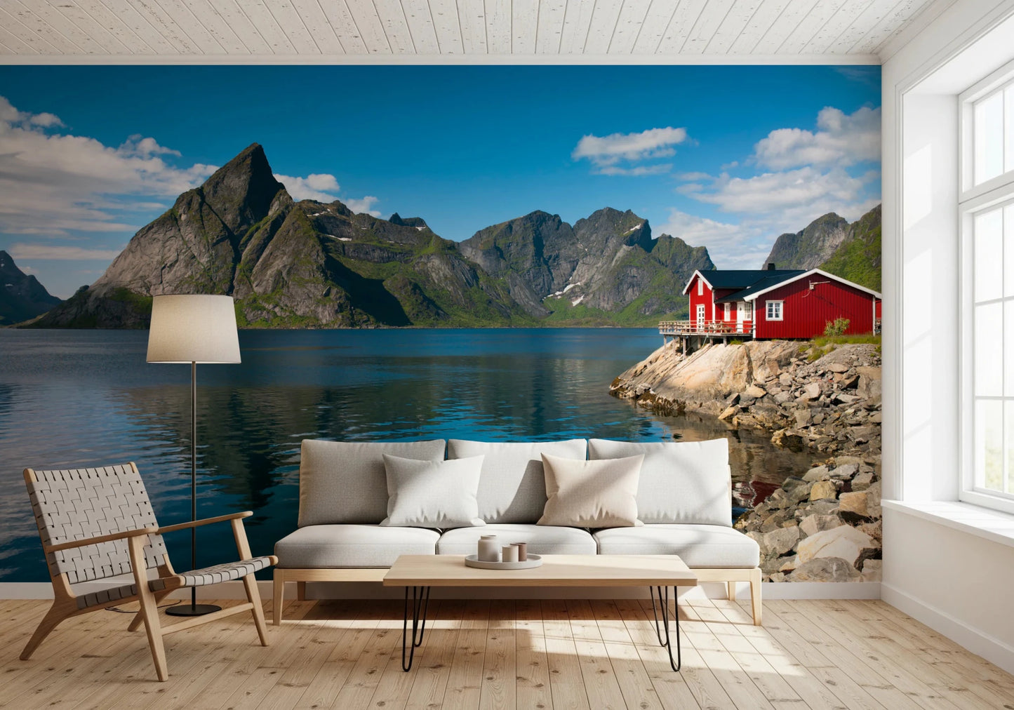 Fishing huts wallpaper mural of a blue fjord and red huts behind a white sofa and woven leather chair in a living room