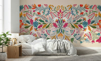 Frida's Garden wallpaper mural of bright folk flowers behind a white bed and wood nightstand