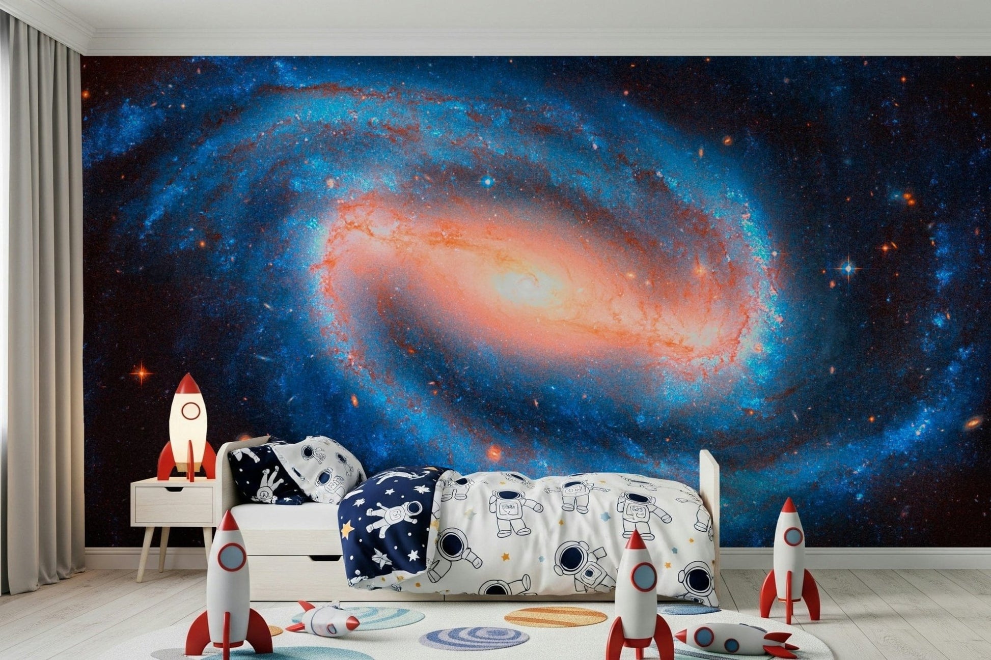 Galaxy Dream wallpaper mural of an orange-cored galaxy behind a kids bed with astronaut bedding and rockets