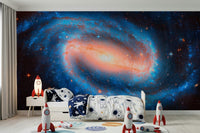 Galaxy Dream wallpaper mural of an orange-cored galaxy behind a kids bed with astronaut bedding and rockets