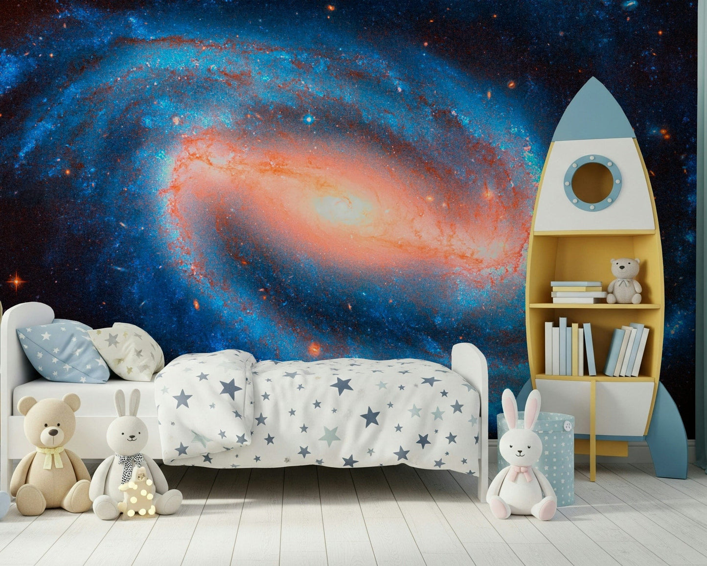 Galaxy Dream wallpaper mural of a spiral galaxy behind a white toddler bed and yellow rocket bookshelf