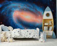 Galaxy Dream wallpaper mural of a spiral galaxy behind a white toddler bed and yellow rocket bookshelf
