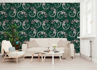 Gecko Groove wallpaper in green with white geckos behind a beige sofa and wood armchair in a living room