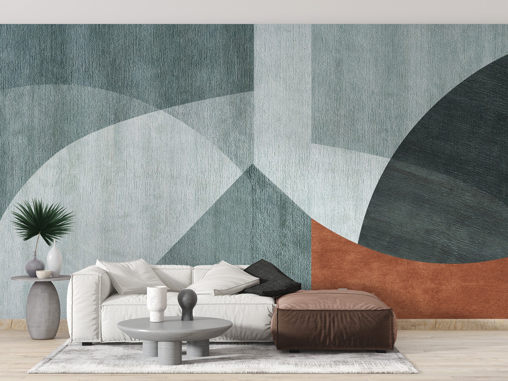 Geometric minimalist wallpaper mural in teal and terracotta shapes behind a white sofa and brown ottoman in a living room