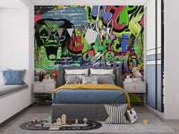 Vibrant Graffiti wallpaper mural in a kids bedroom with a grey bed, blue and mustard bedding and a toy car play rug