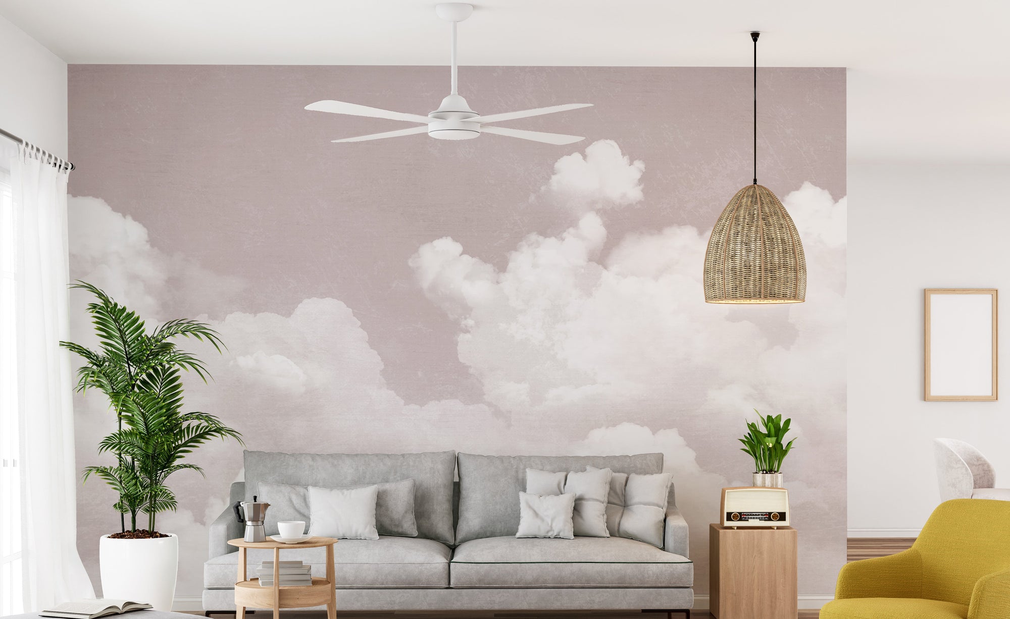 Pink Clouds wallpaper mural of soft white clouds on a dusty pink sky behind a grey sofa and rattan pendant in a living room