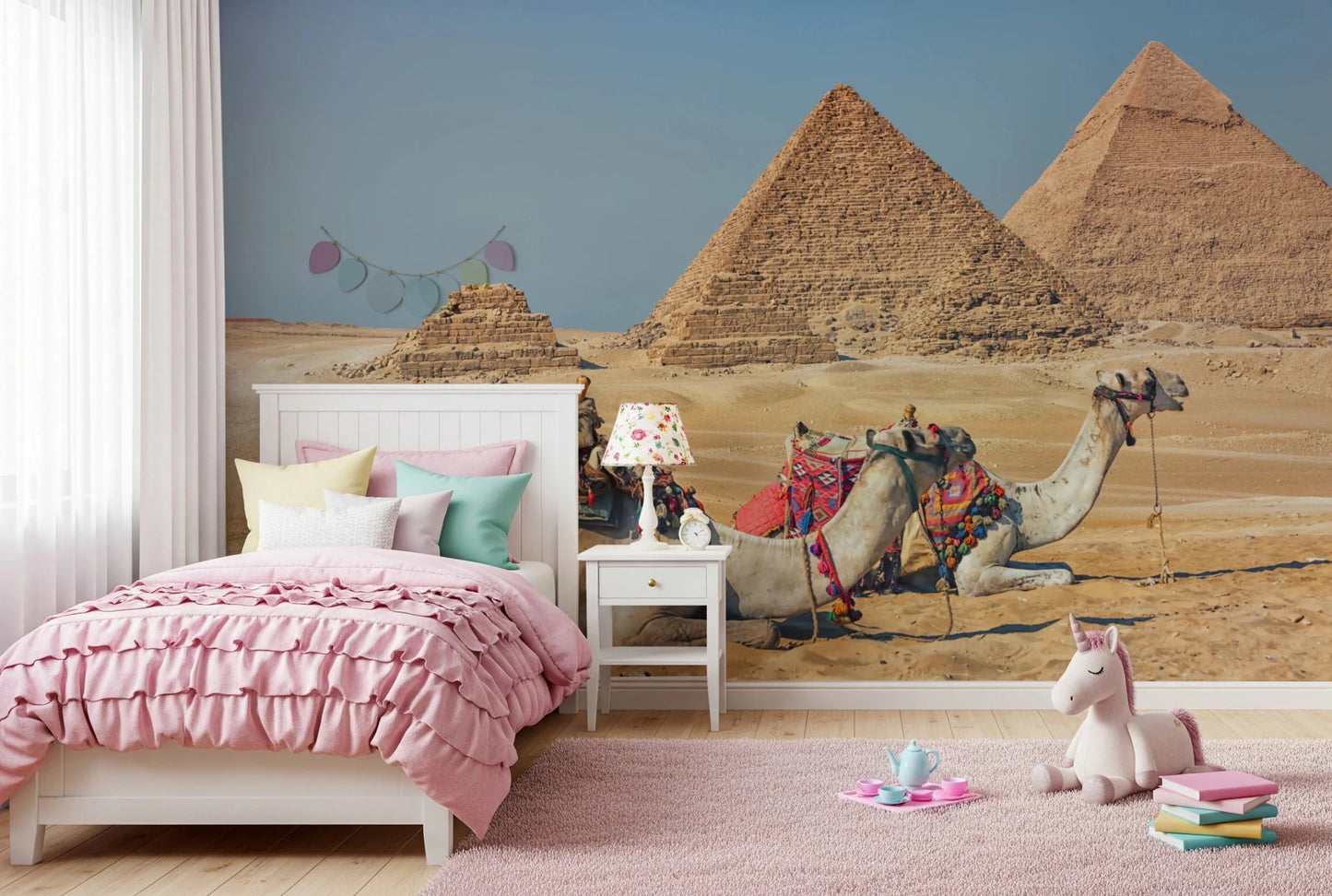 Giza wall mural of the pyramids and saddled camels in a girls room with a pink ruffled bed and unicorn plush