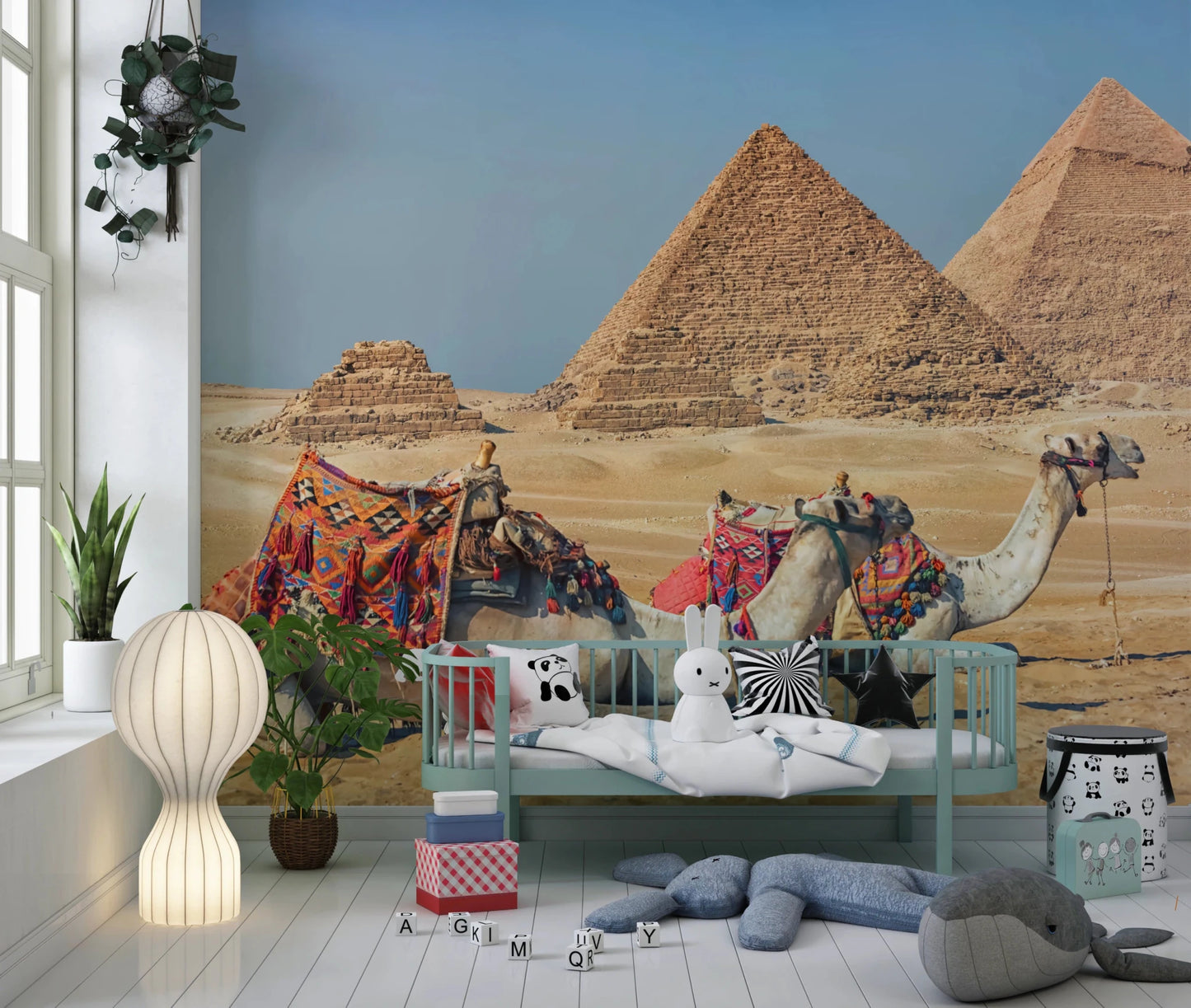 Giza wall mural of the pyramids and camels in a nursery with a mint daybed, plush toys and a paper globe lamp