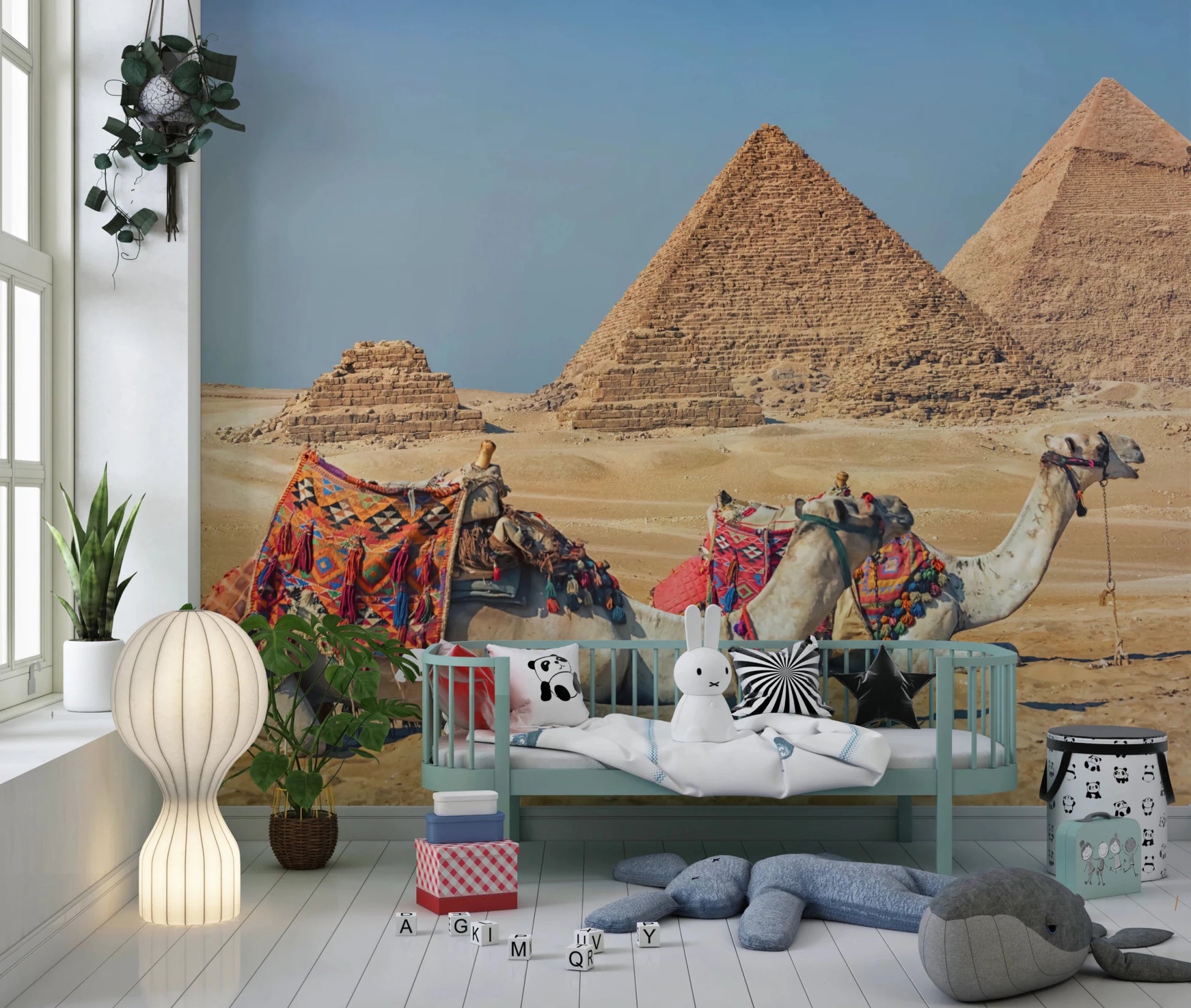 Giza wall mural of the pyramids and camels in a nursery with a mint daybed, plush toys and a paper globe lamp
