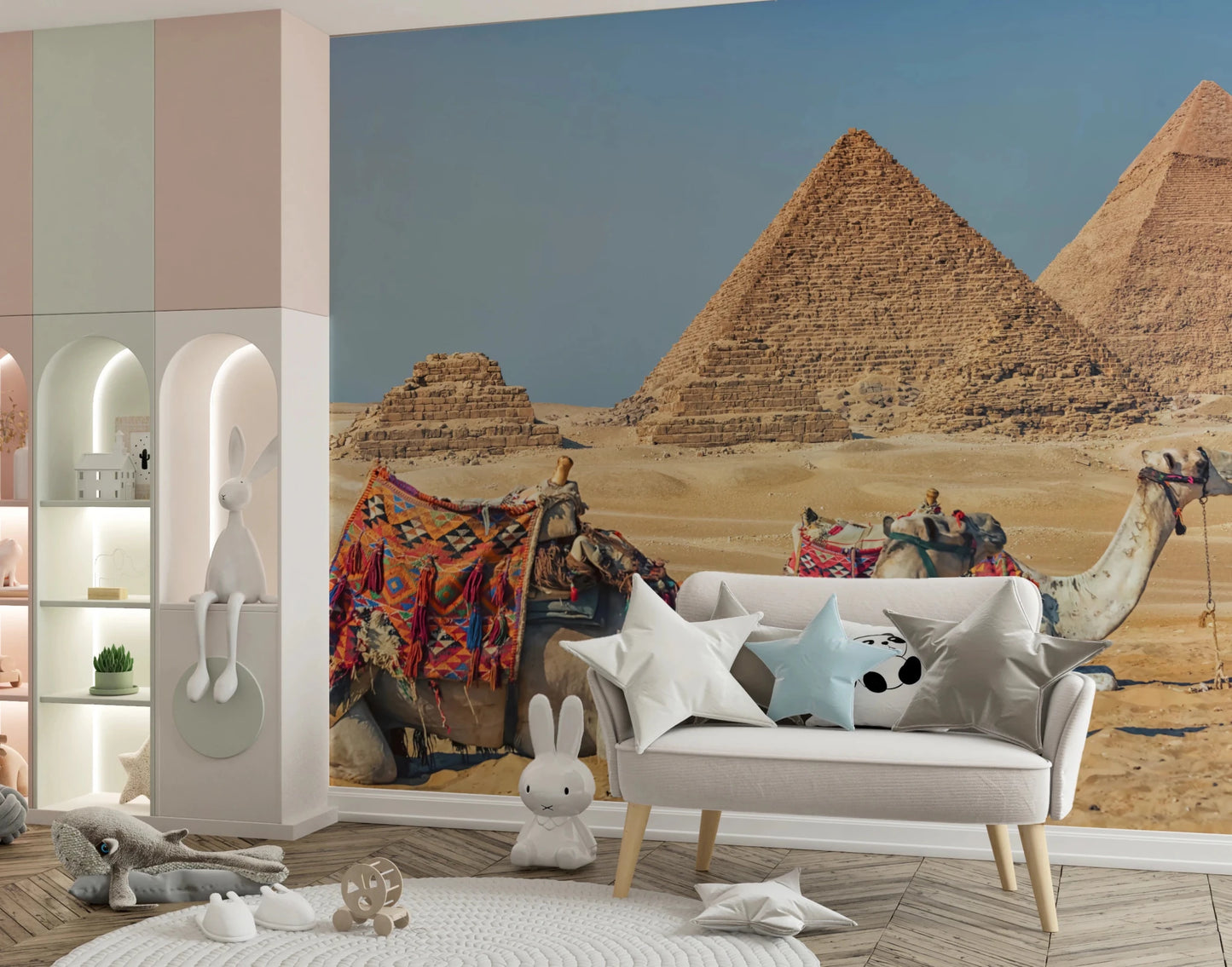 Giza wall mural of the pyramids and camels in a kids room with a white sofa, star pillows and bunny figures
