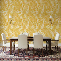 Golden Meadow Dream wallpaper in yellow behind a dark wood dining table with cream chairs and gold sconces