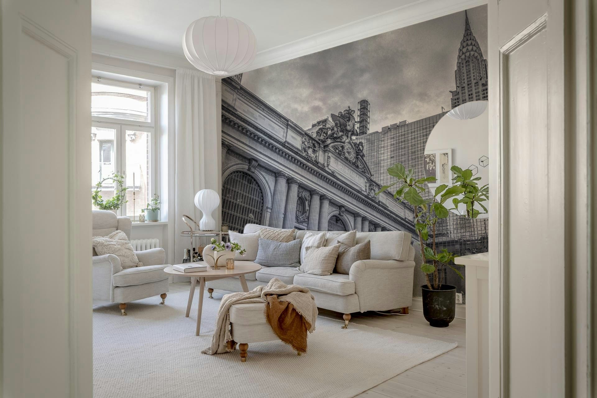 Grand Central Terminal mural in a bright living room with a cream sofa, tall potted plant and pendant lamp