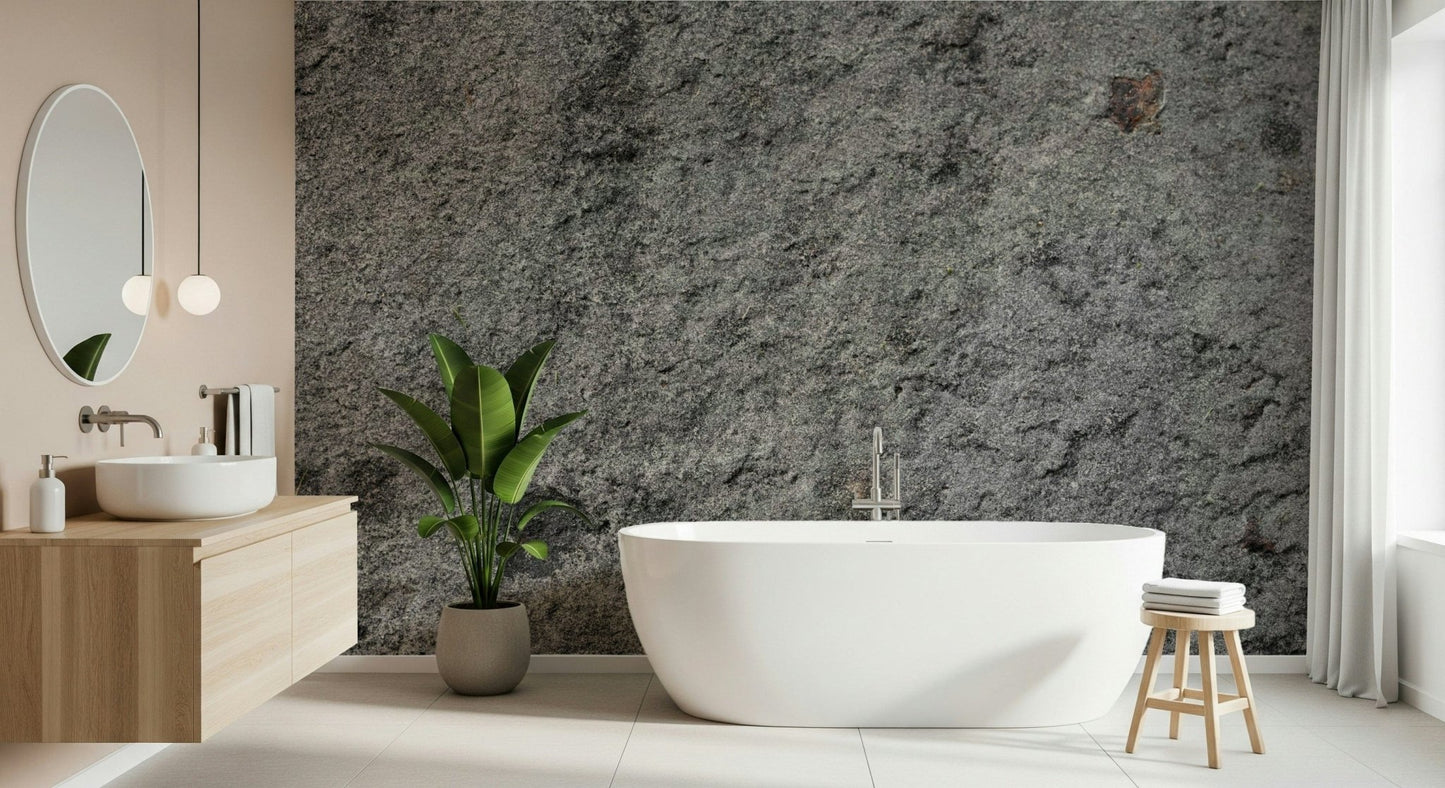 Granite Gray wallpaper mural behind a white freestanding tub, wood vanity and banana-leaf plant in a bathroom