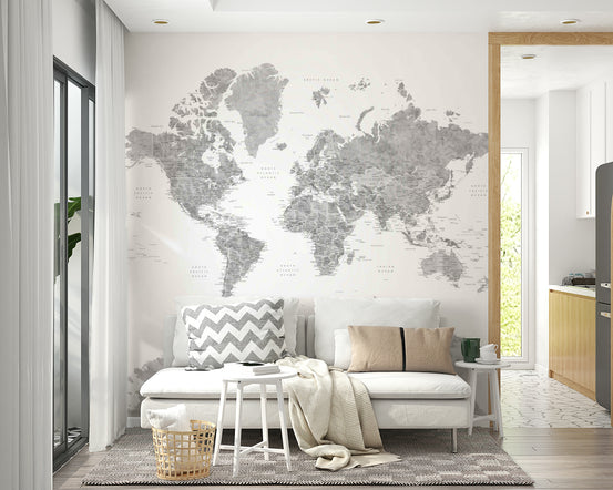 Gray Watercolor World Map wallpaper mural in soft gray behind a white sofa with a grey chevron pillow