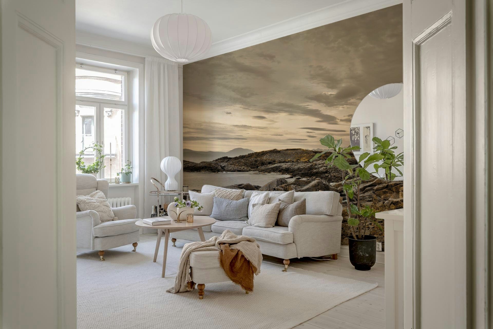 Dramatic wall mural of a lighthouse on a rocky coast with mountains in the distance.