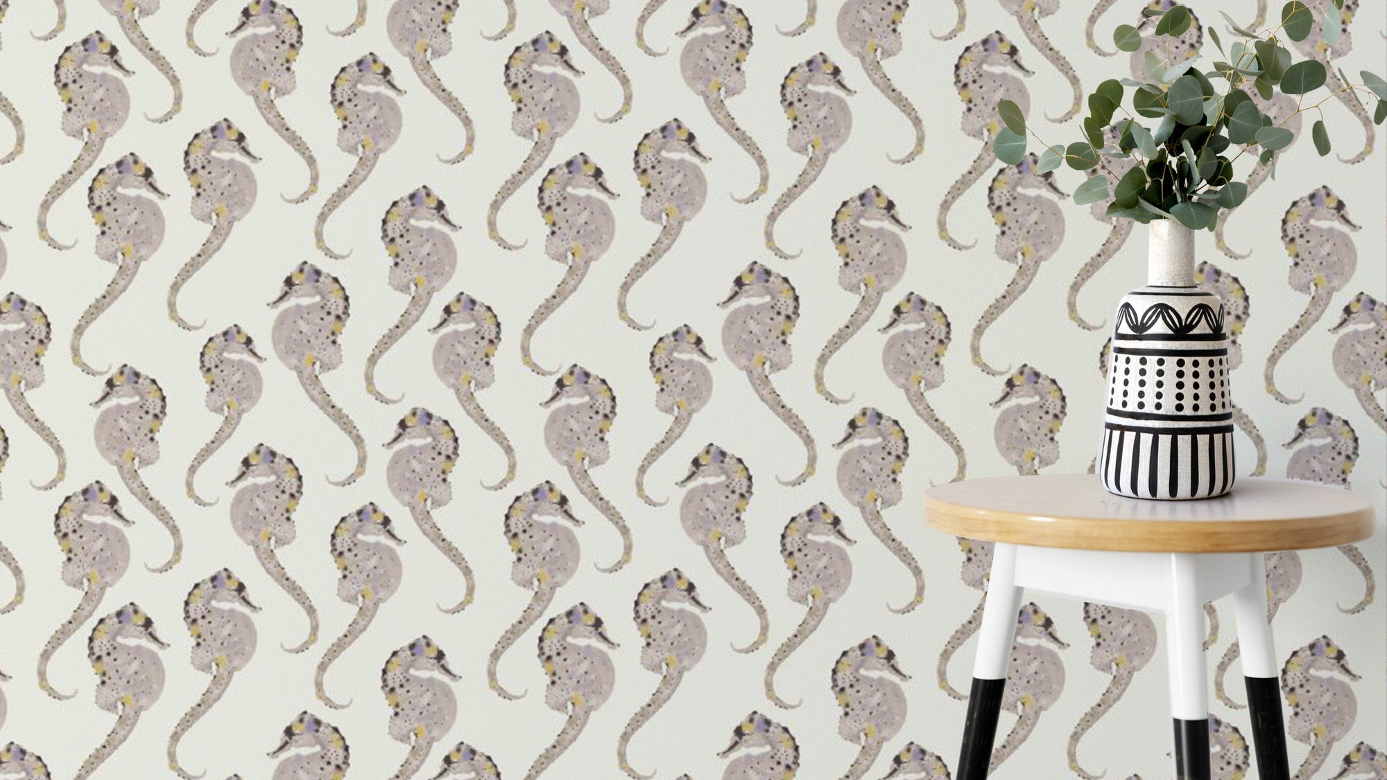 Hippocampus wallpaper with taupe seahorses on cream behind a white stool holding a striped vase and eucalyptus