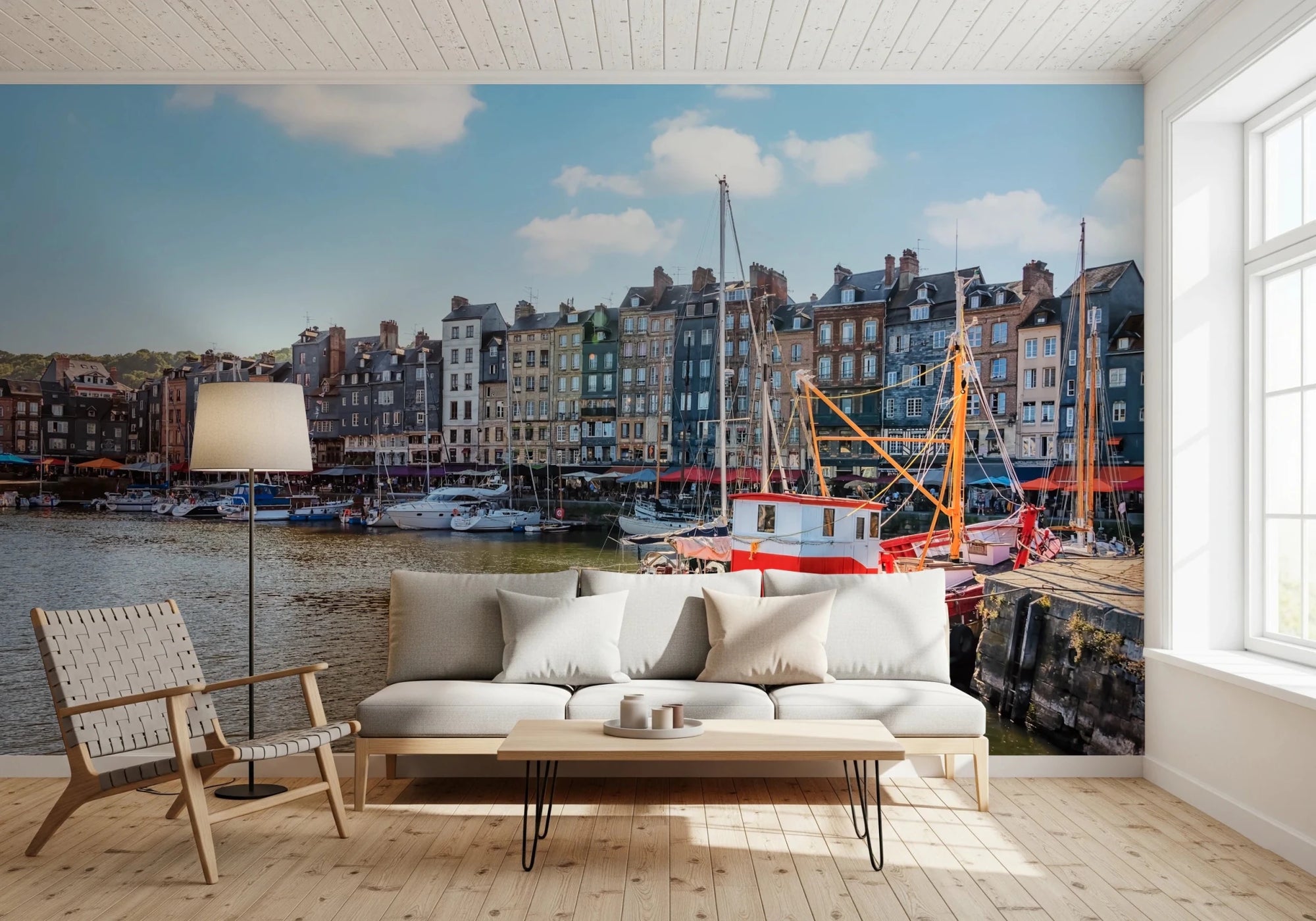 Honfleur Harbor Charm wallpaper mural of the harbor townhouses and red fishing boat behind a white sofa and woven chair