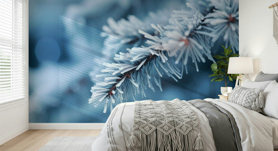 Icy Branch Serenity wallpaper mural of a frosted blue pine branch behind a white bed with a macrame throw in a bedroom