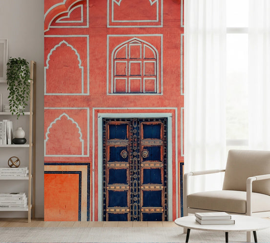Indian Archway wallpaper mural with coral facade and navy studded door beside a beige armchair in a living room
