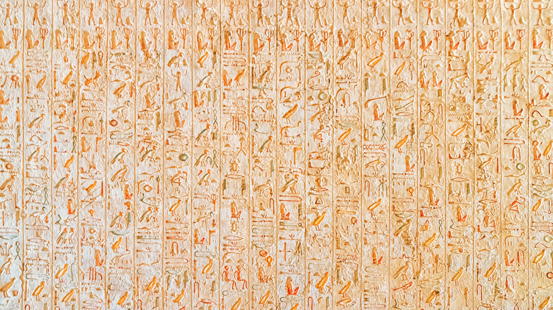 Ancient Inscriptions wallpaper mural in orange hieroglyphics behind an off-white sectional sofa in a sunlit living room