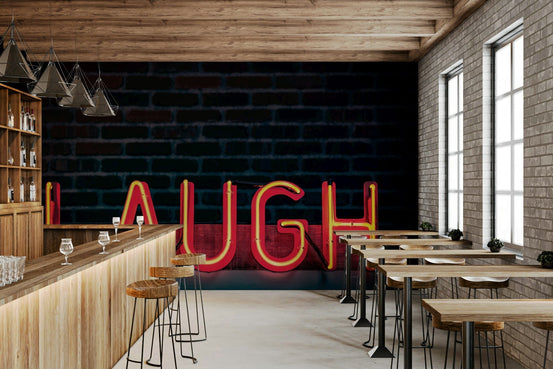 Laugh Neon Glow wallpaper mural of a red LAUGH neon sign on dark brick behind a wood bar and stools in a cafe
