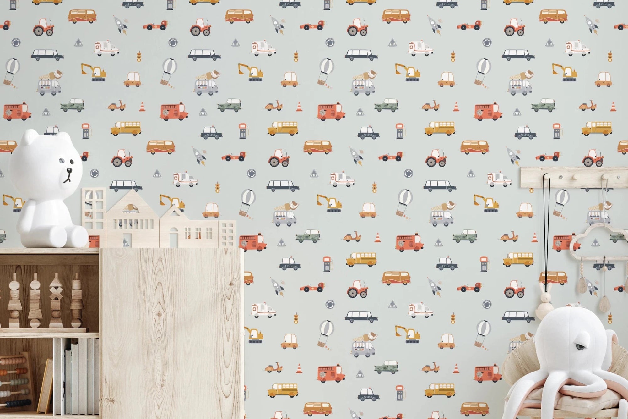 Little Transports in blue wallpaper mural in a nursery with a white teddy lamp and wooden console, soft sage cars and trucks
