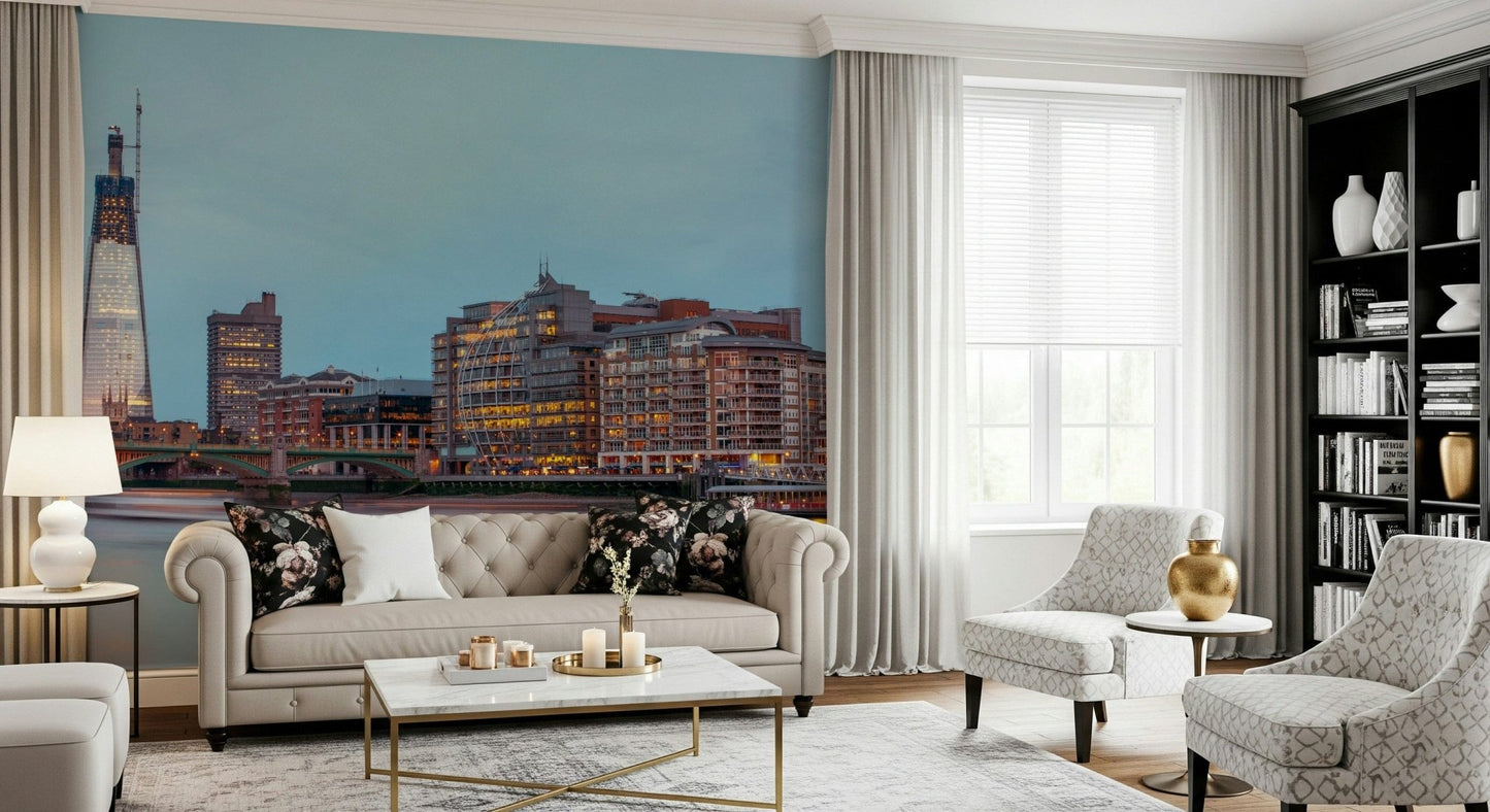 London Luminescence wallpaper mural of the Thames at dusk above a tufted beige sofa and bookshelf in a living room
