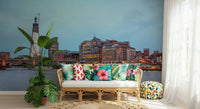 London Luminescence wallpaper mural of the lit London skyline behind a rattan sofa with tropical hibiscus pillows