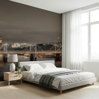 London's Nightfall wallpaper mural of the floodlit Thames bridge behind a white bed and lamp in a bright bedroom