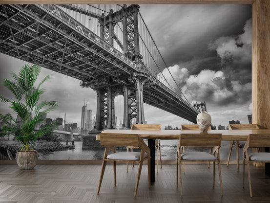 Manhattan Bridge NY City wallpaper mural in black and white behind a wood dining table and chairs with a potted palm