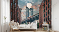 Manhattan Bridge Vista wallpaper mural of the bridge at dusk behind a white bed and rattan chair in a bedroom