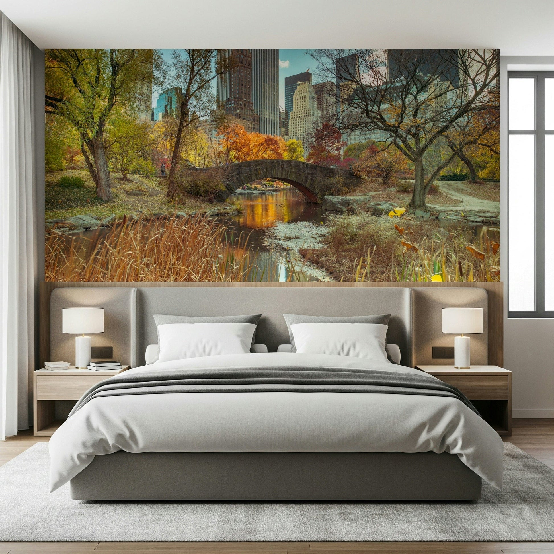 Manhattan's Autumn Embrace wallpaper mural of the park bridge and skyline behind a grey upholstered bed in a bedroom