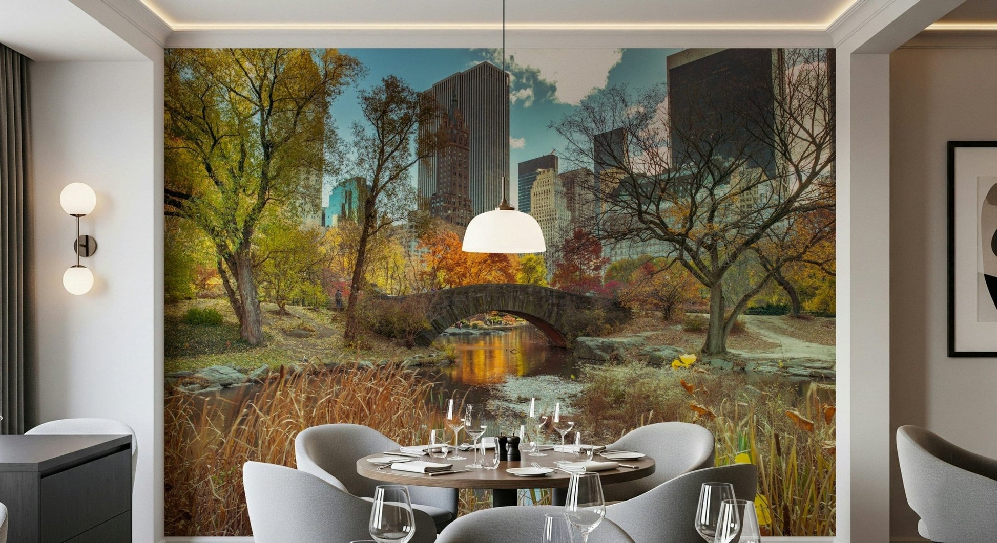 Manhattan's Autumn Embrace wallpaper mural of Central Park's stone bridge behind a round dining table and grey chairs