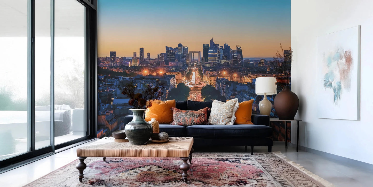 Metropolis Dusk wallpaper mural showing a city skyline at twilight behind a navy sofa with orange pillows in a living room
