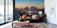 Metropolis Dusk wallpaper mural showing a city skyline at twilight behind a navy sofa with orange pillows in a living room