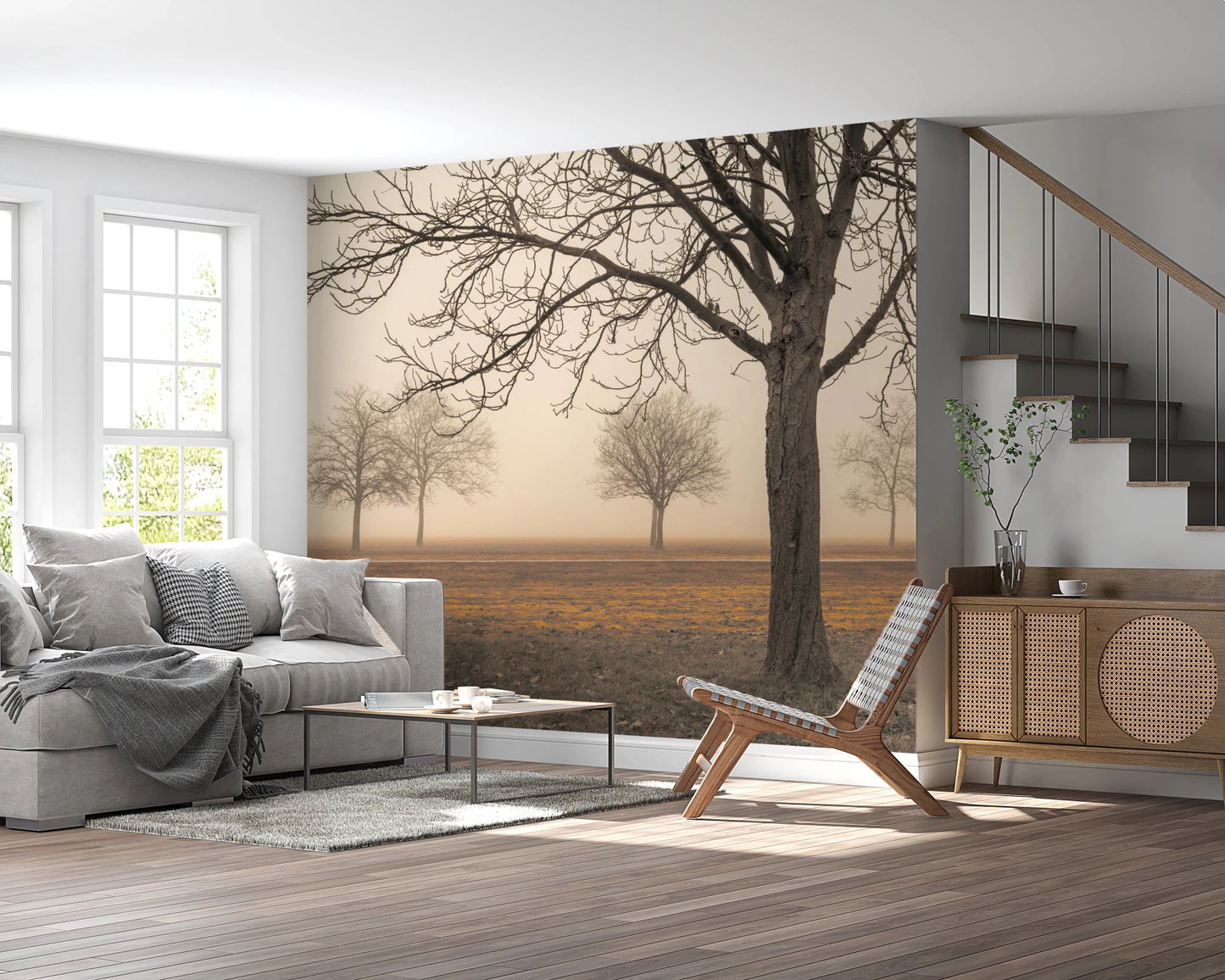 Misty Countryside wallpaper mural of foggy bare trees above a grey sofa and rattan sideboard beside a staircase
