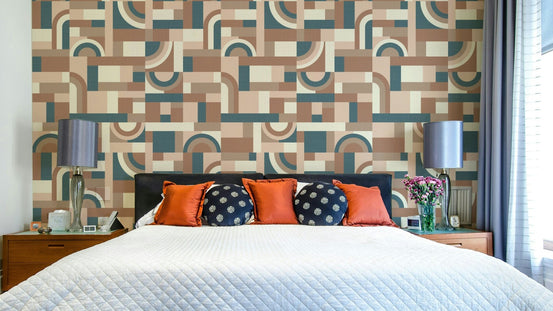 Mocha Mousse Accento wallpaper with retro geometric shapes behind a bed with orange and navy pillows and twin lamps