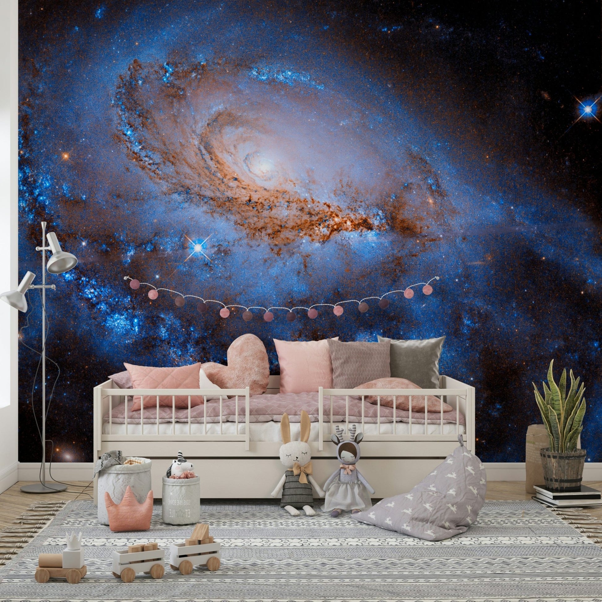 Nebula Dreams wall mural of a blue galaxy behind a white daybed with pink cushions and plush toys in a kids room