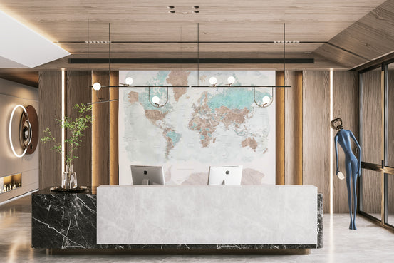 Neutral Watercolor World Map wallpaper mural in teal and brown behind a marble reception desk with two iMacs