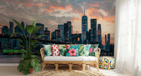 New York In The Evening wallpaper mural of the dusk skyline behind a rattan sofa with tropical floral cushions