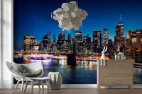 Night Metropolis wallpaper mural of the city at night behind a grey rattan armchair and wood dresser in a living room