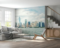 NYC Skyline View wallpaper mural of the harbor skyline behind a grey sofa and cane sideboard by a staircase