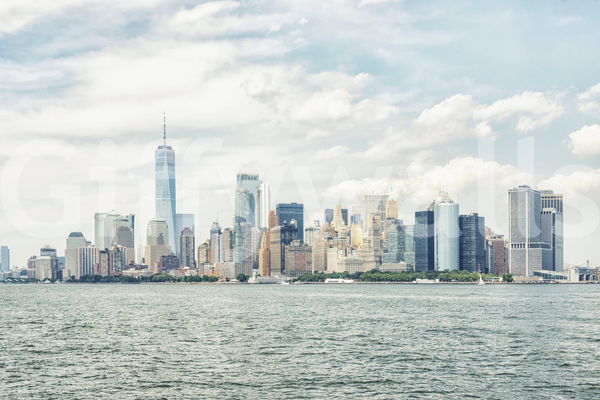 NYC Skyline View wallpaper mural shown as a full-wall view of Lower Manhattan across the harbor under a cloudy blue sky