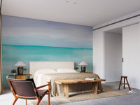 Turquoise Ocean wallpaper mural in a bedroom with a beige upholstered bed, table lamps and a live-edge wooden bench
